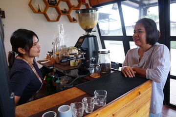 A casual and friendly conversation between the customer and the barista while leaning on the warm wooden counter of the café.