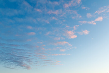 The sky is filled with delicate pastel clouds at dawn or sunset. Pink and purple hues contrast softly against the blue sky. A small crescent moon is visible near the horizon.