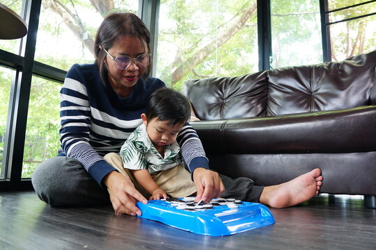 A woman wearing glasses is helping a small child play checkers or a similar board game.