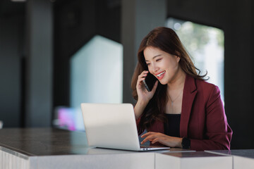 Young businesswoman talking on phone and working on laptop