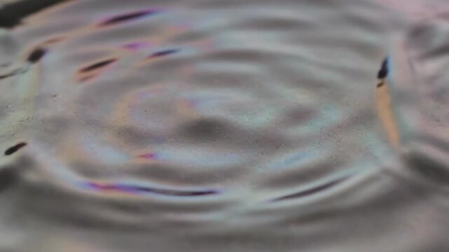 Shimmering slow-motion surface texture of iridescent silver fluid creates gentle concentric resonant ripples moving outward meditative, metallic sheen, fluid motion
