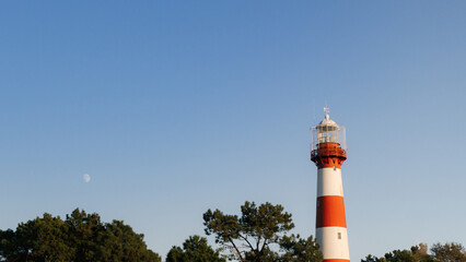 red and white lighthouse with moon in clear blue sky