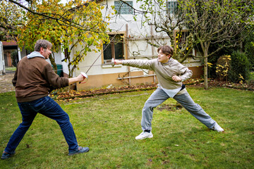 teenage boy and father practice fencing with a saber, teenager wearing a fencing uniform outdoors.