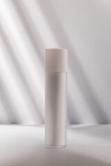 Grey bottle on a white surface, with diagonal shadows creating a stark, modern aesthetic.