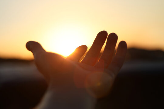 A hand reaching out toward the brightly rising sun, a New Year's sunrise background filled with hope for a brighter tomorrow and hopes and aspirations.
