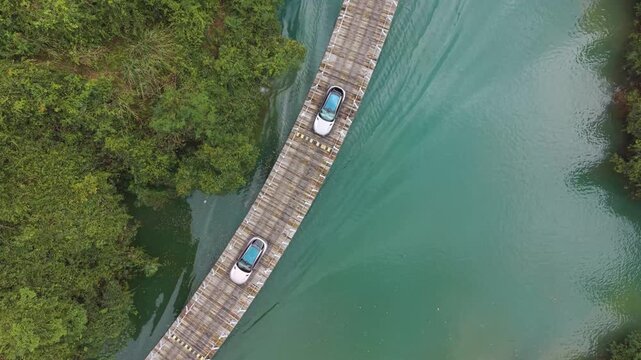 Top-down drone shot of the Shiziguan floating bridge in Hubei, China, showing cars crossing over green river water surrounded by dense forest and mountains.