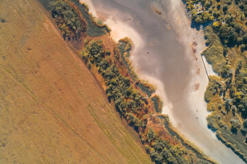 Aerial drone shot showing land use contrast between a cultivated field and a dry riverbed. The riparian zone creates a sharp ecological boundary, illustrating drought impact.