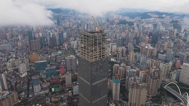Orbiting drone shot of the massive Hengfeng Guiyang Center Tower 1 under construction, with the cityscape of Guiyang, China.