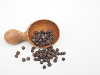 Several black peppercorns placed in a wooden spoon  on white background. Healthy food seasoning.