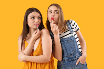 Female friends applying lipsticks on yellow background