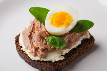 Smorrebrod garnished with tuna, eggs, cream cheese on rye bread served on a white plate. Traditional Danish open-faced sandwich.