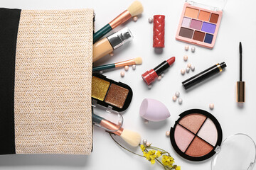 Stylish cosmetic bag with makeup products and beautiful flowers on white background