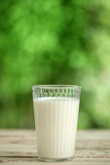 Glass of fresh milk on white wooden table outdoors