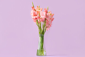 Glass vase with bouquet of beautiful gladiolus flowers on lilac background