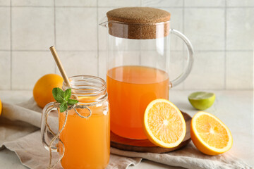 Mason jar and jug of fresh orange juice with mint on white table