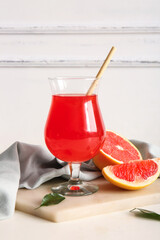 Board with glass of tasty grapefruit juice and fresh fruits on light table