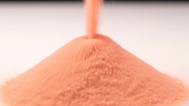 Ultra close-up cinematic slow motion shot of fine pastel peach colored sand flowing down to form a smooth minimalist conical pile shape, flow, pile