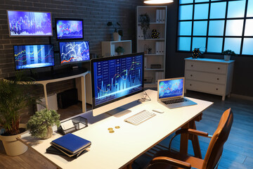 Computer and laptop with stock data on trader's desk in dark office at night