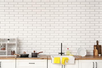 Wooden kitchen counter with clean dishes and cleaning supplies near light brick wall