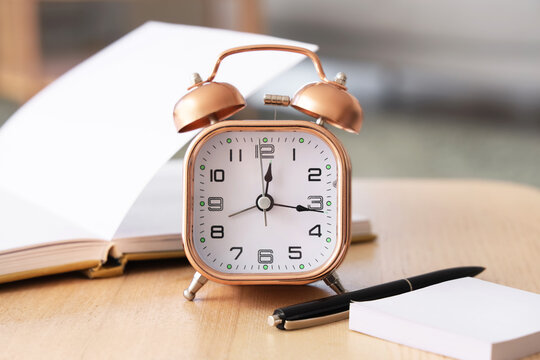 Alarm clock with notebook and pen on table in living room, closeup