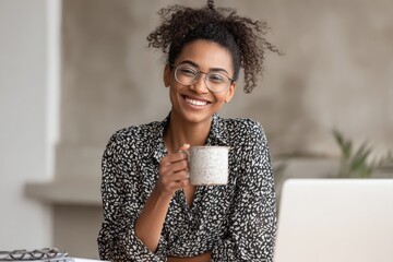 Happy African American businesswoman enjoys a cup of coffee during a productive workday in a modern office setting filled with natural light and greenery