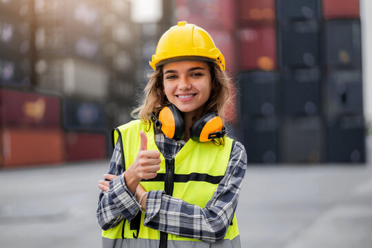 A woman wearing a yellow vest and a hard hat is smiling and giving a thumbs up