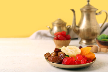 Plate with different candied fruits and teapot on white table