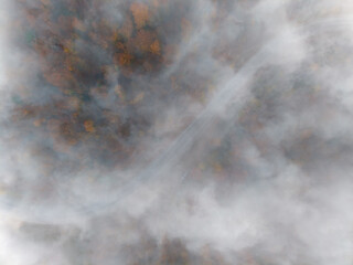 Faint road disappears into swirling fog above a forested landscape
