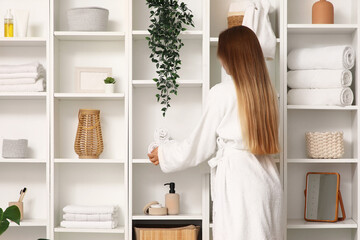 Obraz premium Young woman with towels on shelf unit in bathroom, back view