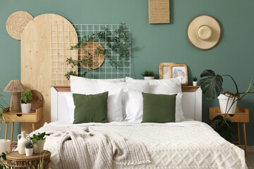 Big comfortable bed, tables and houseplants in stylish interior of bedroom, closeup