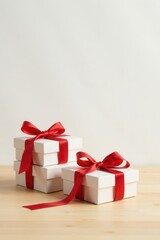 Obraz premium A stack of pristine white gift boxes adorned with vibrant red ribbons, resting elegantly on a light wooden surface against a minimalist white backdrop