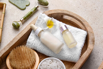 Wooden tray with towel, massage body brush and bottles of cosmetic products on white grunge background, closeup