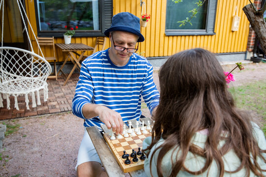 Father and tween daughter playing chess in their backyard on a summer day. Quality family time and mental development in a relaxed outdoor setting.