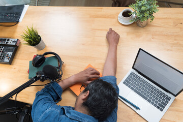 Tired man sleeping on work desk with laptop, microphone and headphones showing creative burnout concept