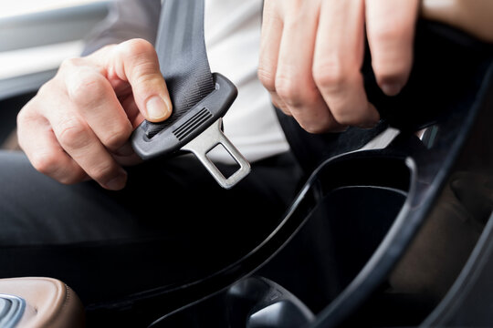 Close-up of driver fastening seatbelt for road safety, showing hand buckling belt inside modern car interior