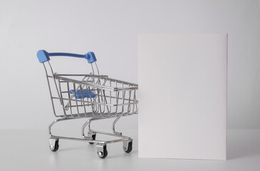 Toy metal supermarket trolley with white paper card for informstion on white background. Buying, sale concept. Mockup for design
