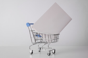 Toy metal supermarket trolley with white paper card for informstion on white background. Buying,...