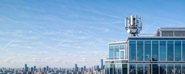 Telecommunications tower with 5G and 6G antennas on a modern building roof. Urban city skyline background with blue sky. Wireless network technology concept with copy space