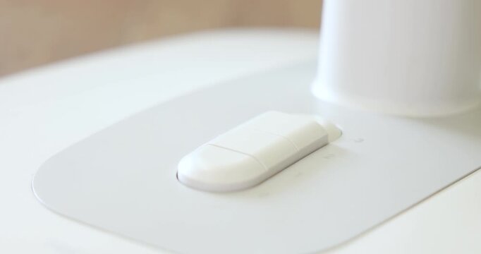 A hand presses a large, white, speed-control fan button on the base of a modern, minimalist fan or appliance, adjusting the settings for airflow or temperature in a bright room. 4k VDO.