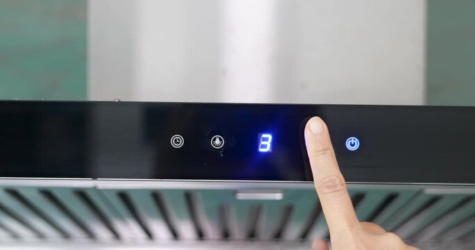 A hand presses a glowing blue touch kitchen hood control button on the digital display of a modern black kitchen range hood, adjusting the fan speed for cooking ventilation. 4k VDO.