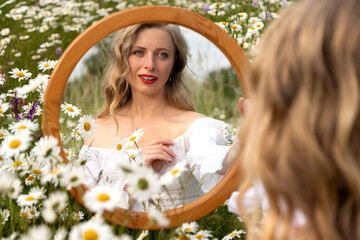 Chamomile field. Woman with a mirror. Photo of young girl face with care of her face in mirror