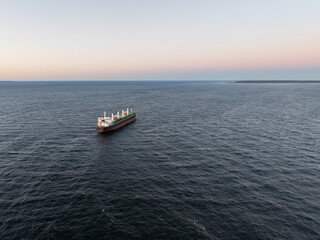 Fototapeta premium Aerial view of a large bulk carrier cargo ship sailing in the calm Baltic Sea during a peaceful pink sunset.