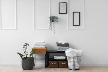 Coffee tables with baskets, bed sheets and houseplants near white wall in living room