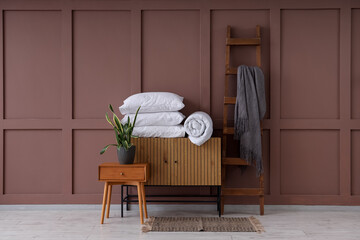 Commode with coffee table, blanket and pillows near brown wall in living room