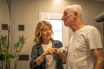 Mature woman applying hydrating cream on man's face, practicing a wellness skincare routine