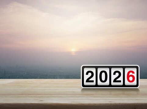Retro flip clock with 2026 text on wooden table over modern city tower and skyscraper at sunset, vintage style, Happy new year 2026 cover concept