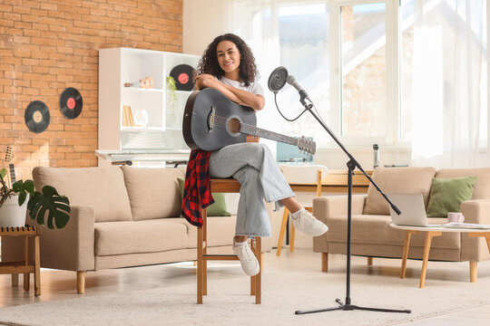 Pretty young African-American woman with microphone and acoustic guitar sitting in living room