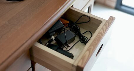 A hand reaches into a wooden desk drawer filled with electronic accessories and tangled cables to retrieve clear safety glasses, preparing for work or DIY eye protection. Concept of safety. 4k VDO.