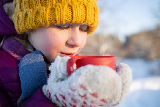 A child drinks hot tea from a thermos cup outdoors in a park during the Christmas holidays in winter.