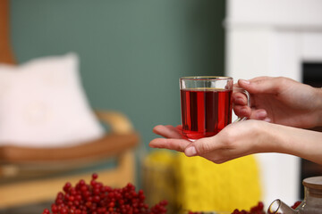 Young woman holding cup of hot viburnum tea at home, closeup